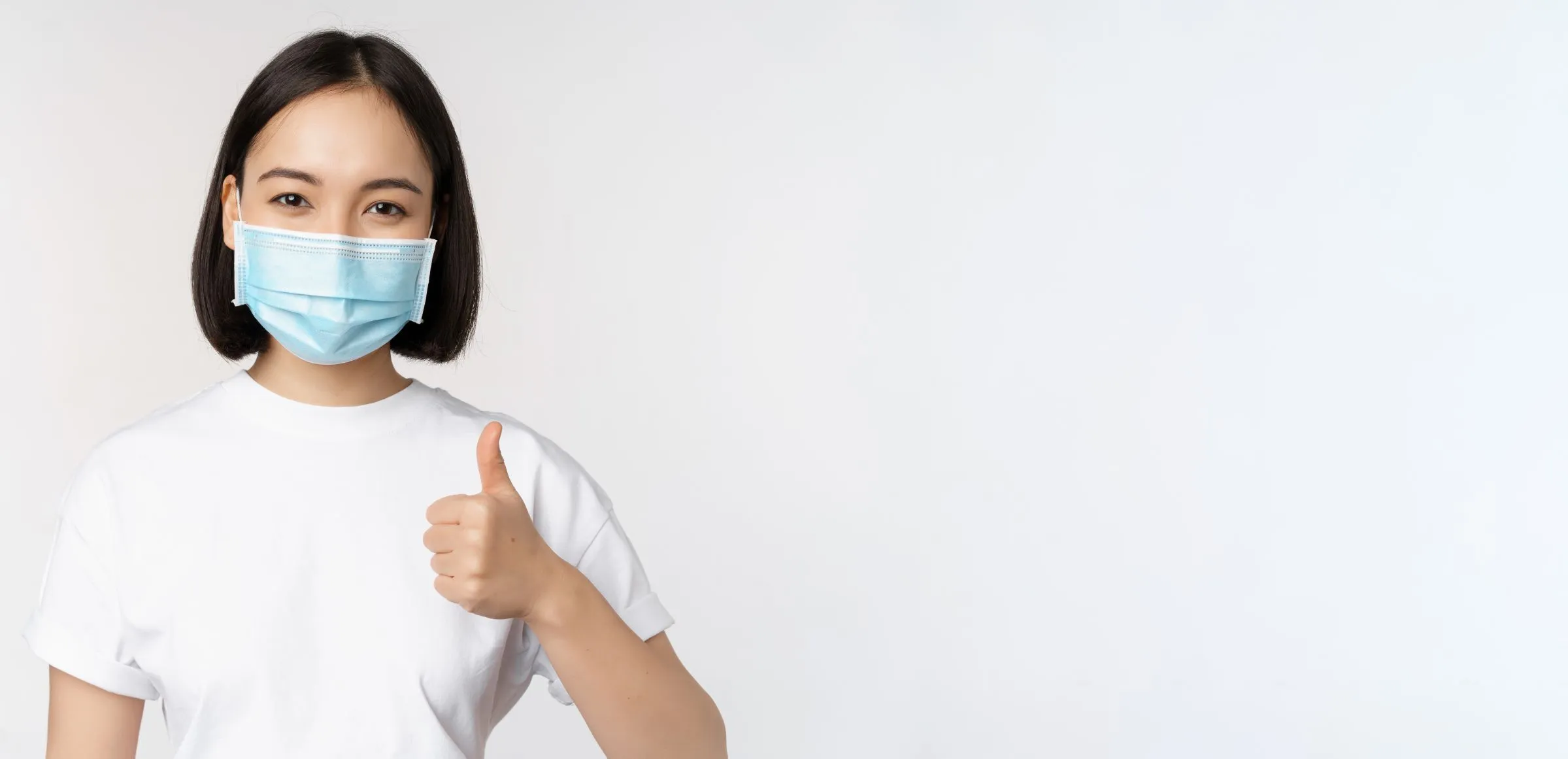 A smiling patient in a surgical mask giving a thumbs up
